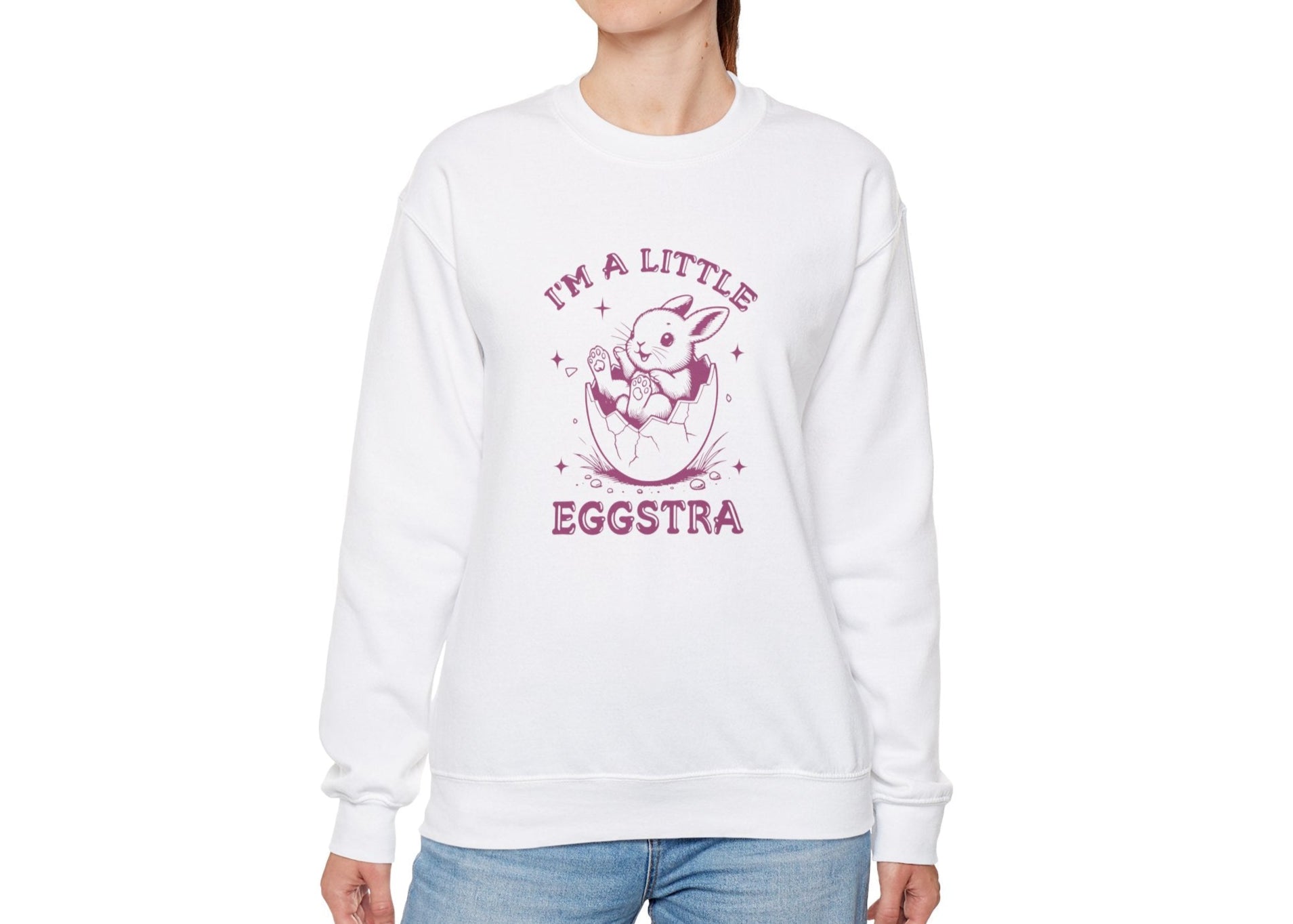 Woman wearing white sweater jumper with pink “I’m a Little Eggstra” Easter graphic. Part of the Vivid Divergence Sensory Friendly Unisex Sweater Jumper Range.