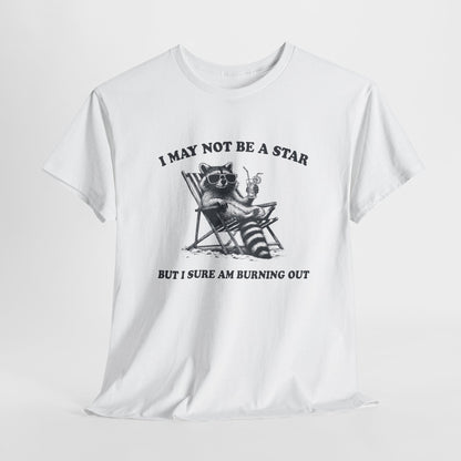 Hanging front view of a white T-shirt featuring a cute raccoon holding a star with text that reads "I May Not Be A Star, But I Sure Am Burning Out." Part of the Vivid Divergence Sensory Friendly Unisex Tees Range.