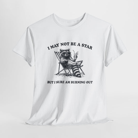 Hanging front view of a white T-shirt featuring a cute raccoon holding a star with text that reads "I May Not Be A Star, But I Sure Am Burning Out." Part of the Vivid Divergence Sensory Friendly Unisex Tees Range.