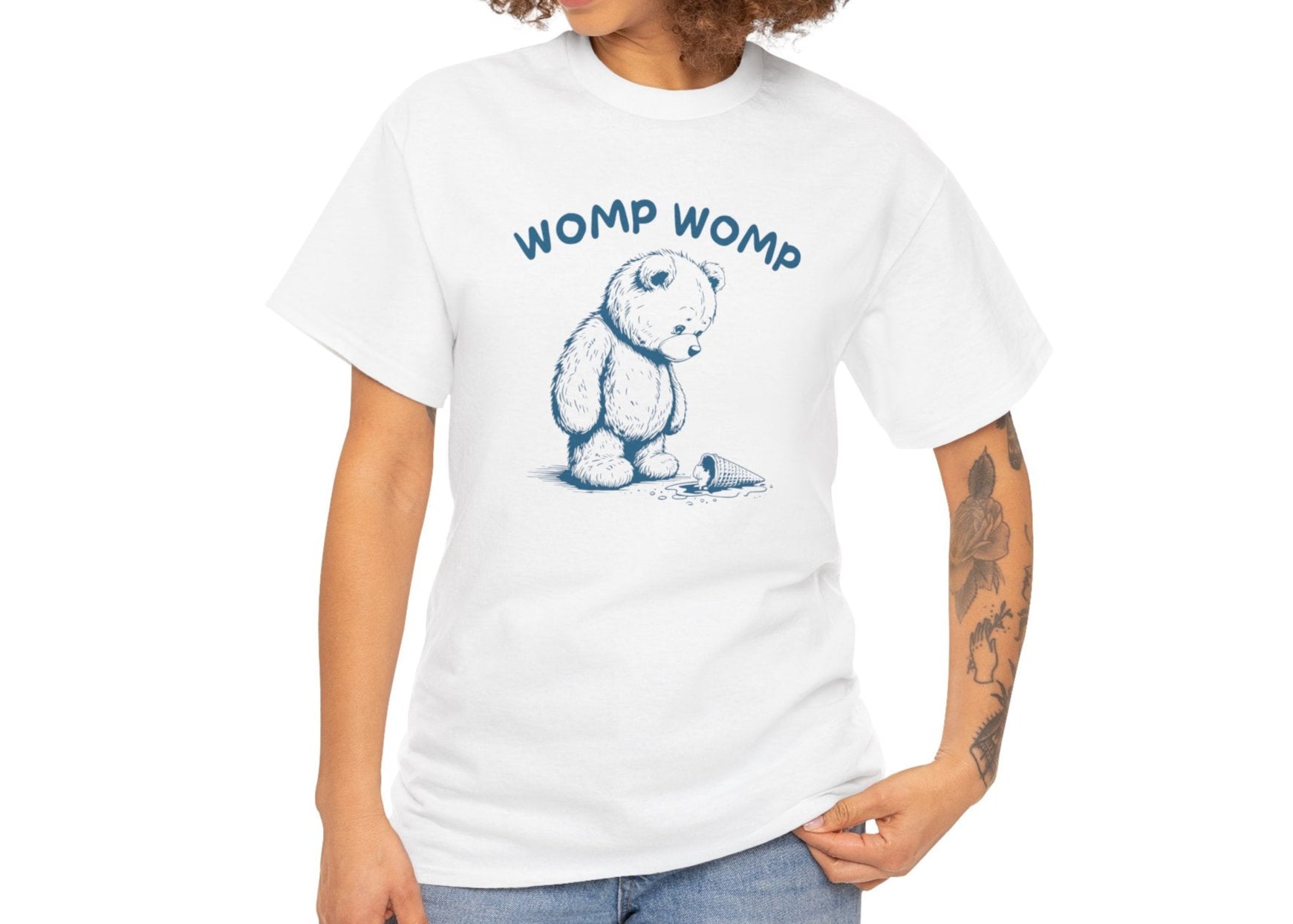 Model with curly hair wearing a white T-shirt featuring "Womp Womp" text with a sad bear looking at a dropped ice cream cone in blue-tone design. Part of the Vivid Divergence Sensory Friendly Unisex Tees Range.