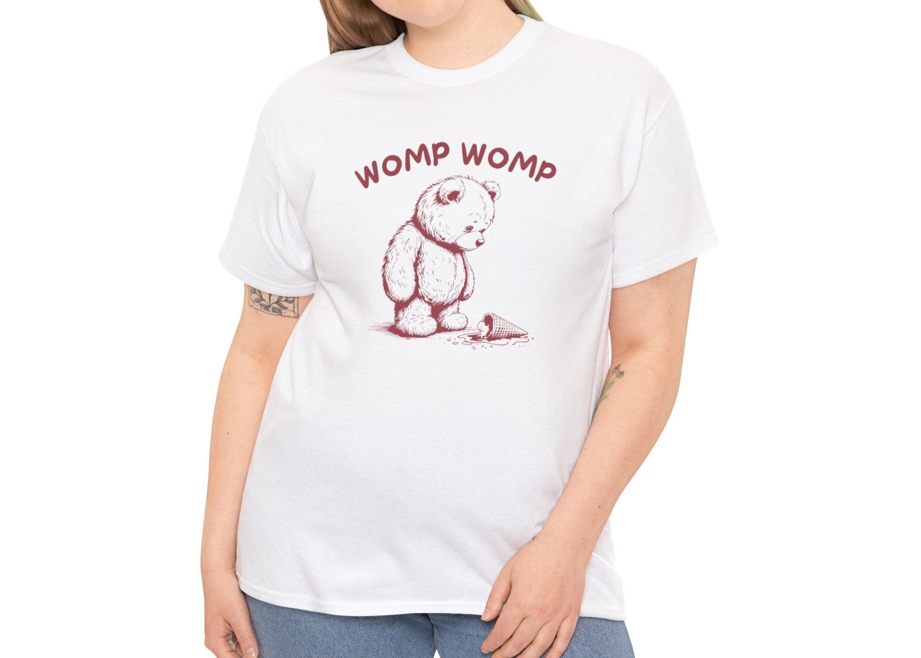 Model wearing a white T-shirt featuring "Womp Womp" text with a sad bear looking at a dropped ice cream cone in red-tone design. Part of the Vivid Divergence Sensory Friendly Unisex Tees Range.