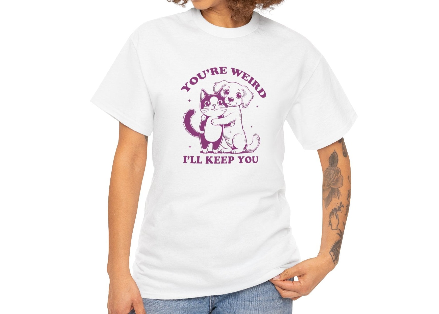 Model with curly hair wearing a white T-shirt with a "You're Weird, I'll Keep You" design featuring a dog hugging a cat in purple. Part of the Vivid Divergence Sensory Friendly Unisex Tees Range.