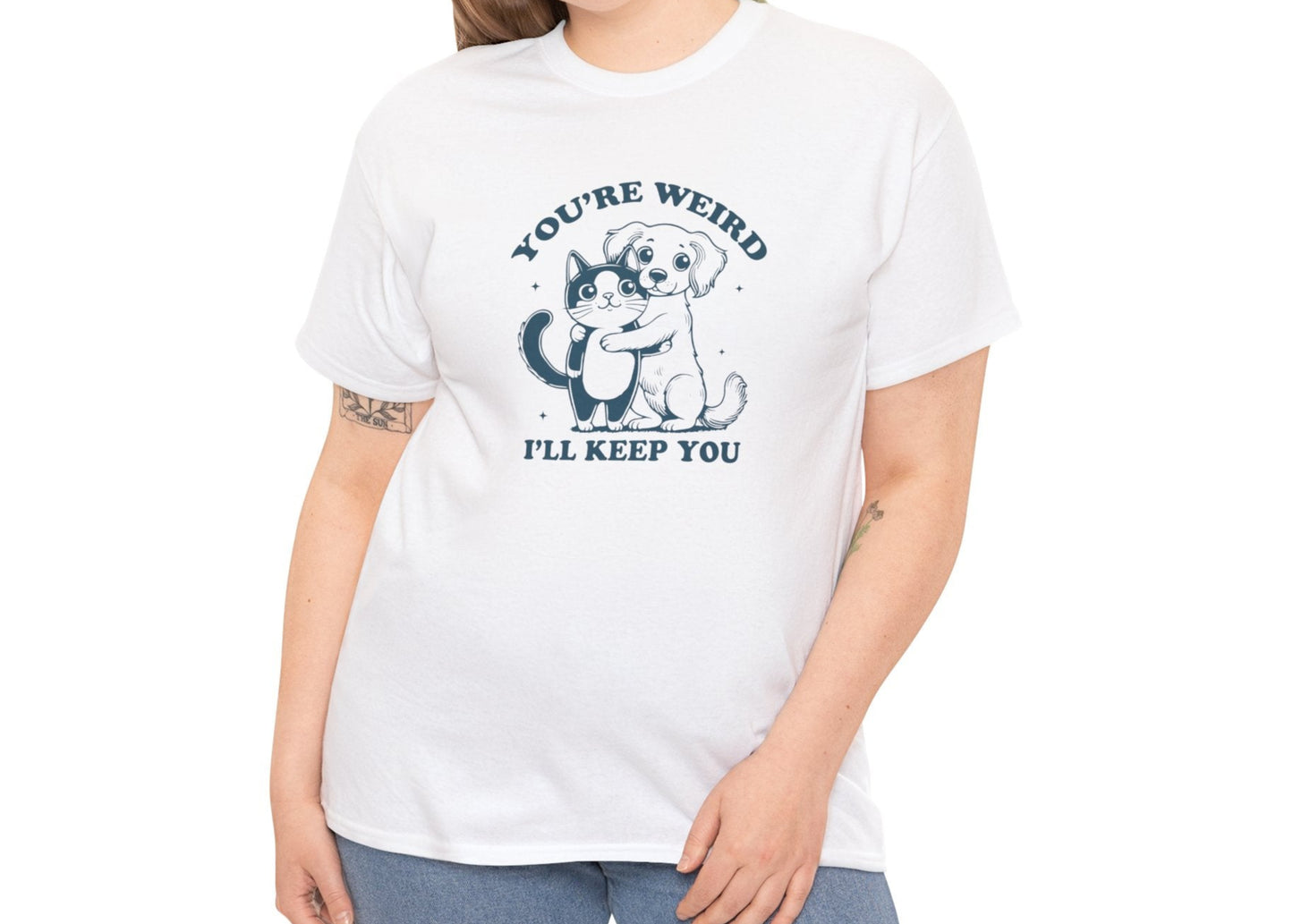 Model wearing a white T-shirt with a "You're Weird, I'll Keep You" design featuring a dog hugging a cat in teal. Part of the Vivid Divergence Sensory Friendly Unisex Tees Range.
