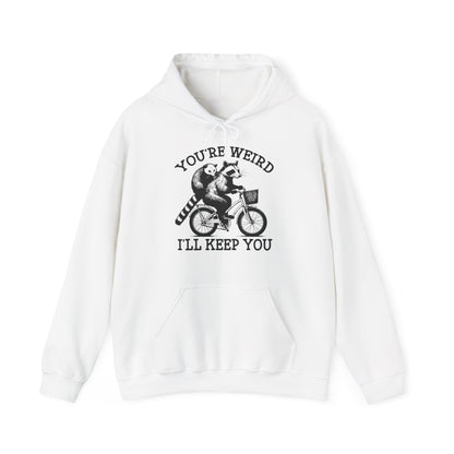Front view of a white hoodie featuring the text "You're Weird, I'll Keep You" with a cartoon illustration of two raccoons riding a bicycle. Part of the Vivid Divergence Sensory Friendly Unisex Hoodie Range.