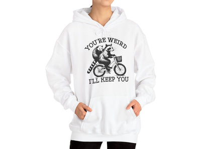 Model wearing a white hoodie featuring the text "You're Weird, I'll Keep You" with a cartoon illustration of two raccoons riding a bicycle. Part of the Vivid Divergence Sensory Friendly Unisex Hoodie Range.