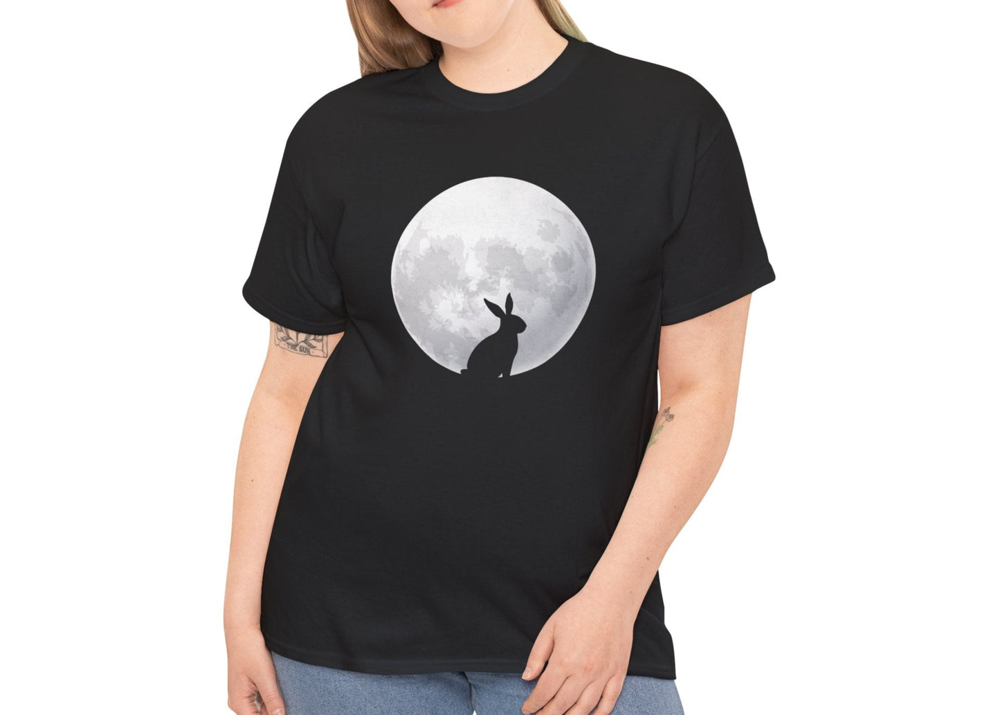 Woman wearing a black Easter T-shirt featuring a rabbit silhouette against a full moon, a stylish and mystical design. Hop into the season in style and shop Easter shirts online today!