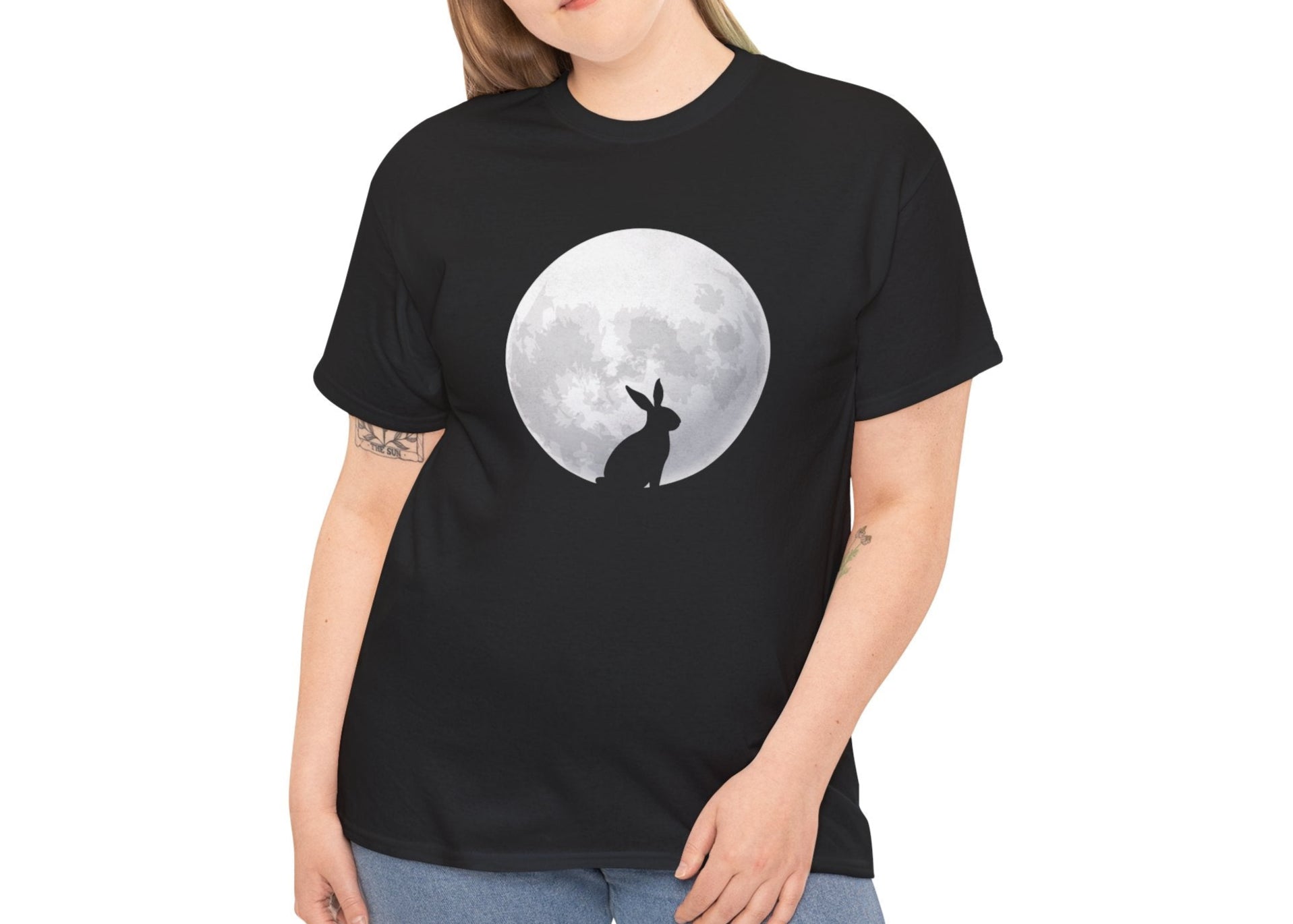 Woman wearing a black Easter T-shirt featuring a rabbit silhouette against a full moon, a stylish and mystical design. Hop into the season in style and shop Easter shirts online today!