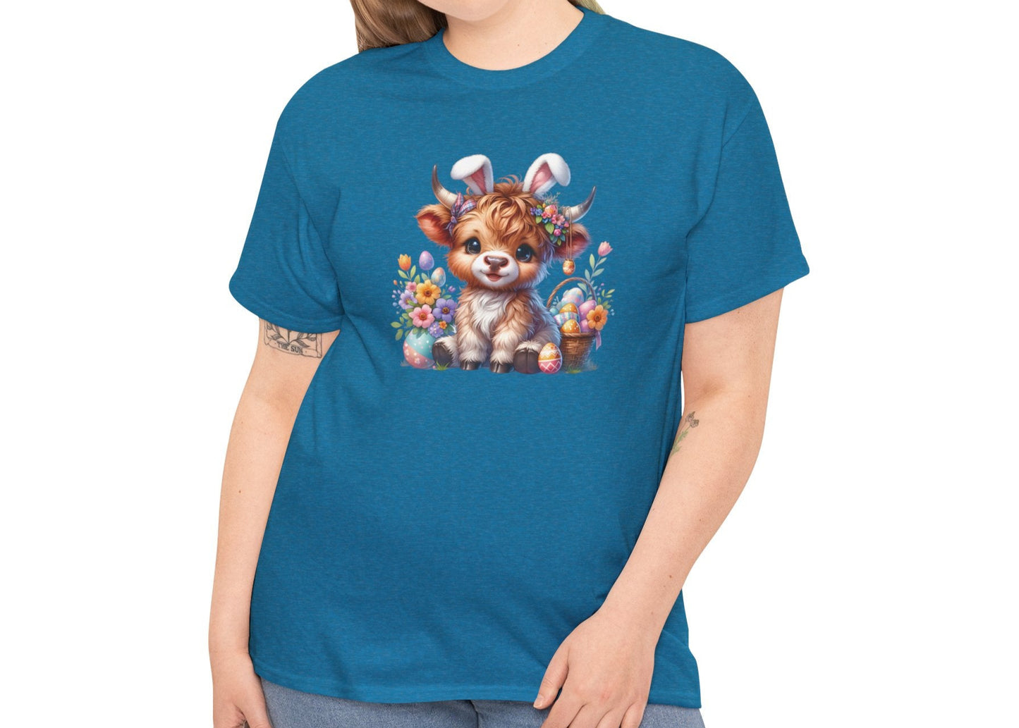 Woman wearing a blue Easter T-shirt featuring a cute Highland cow with bunny ears, Easter eggs, and flowers, a charming holiday outfit. Hop into the season in style and shop Easter shirts online today!