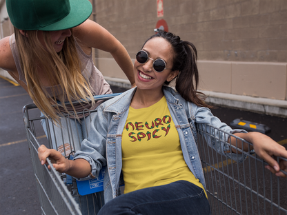 Two individuals outdoors, one wearing a yellow T-shirt with "Neuro Spicy" text, styled casually. Part of the Vivid Divergence Sensory Friendly Unisex Tees Range